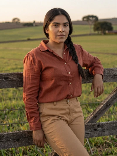 Cynthia, 28, Paraguayan woman from Caaguazú in rust-colored shirt at rural landscape with green fields - Latin 312 verified profile