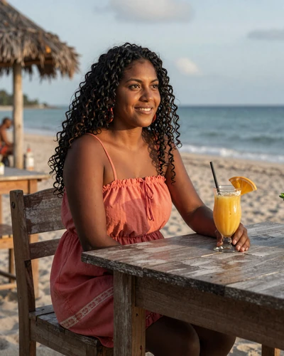 Beautiful Belizean Garifuna woman enjoying tropical refreshment at a beachside table in Dangriga with Caribbean Sea in background